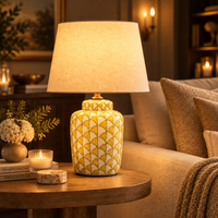 A yellow and white patterned ceramic table lamp with a beige fabric drum shade sits in a  living room 