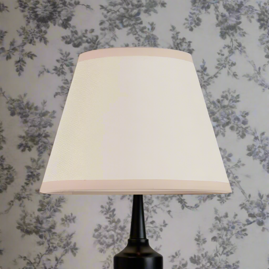 A 20 cm tapered lampshade with a vintage, classic design. The shade is crafted from a light cream textured fabric that gives it a soft, neutral appearance, making it versatile for different interiors. Both the top and bottom edges are neatly finished with matching trim, adding a touch of refinement while maintaining its simple and elegant look. Ideal for table lamps or wall lights, it provides a warm, diffused glow.