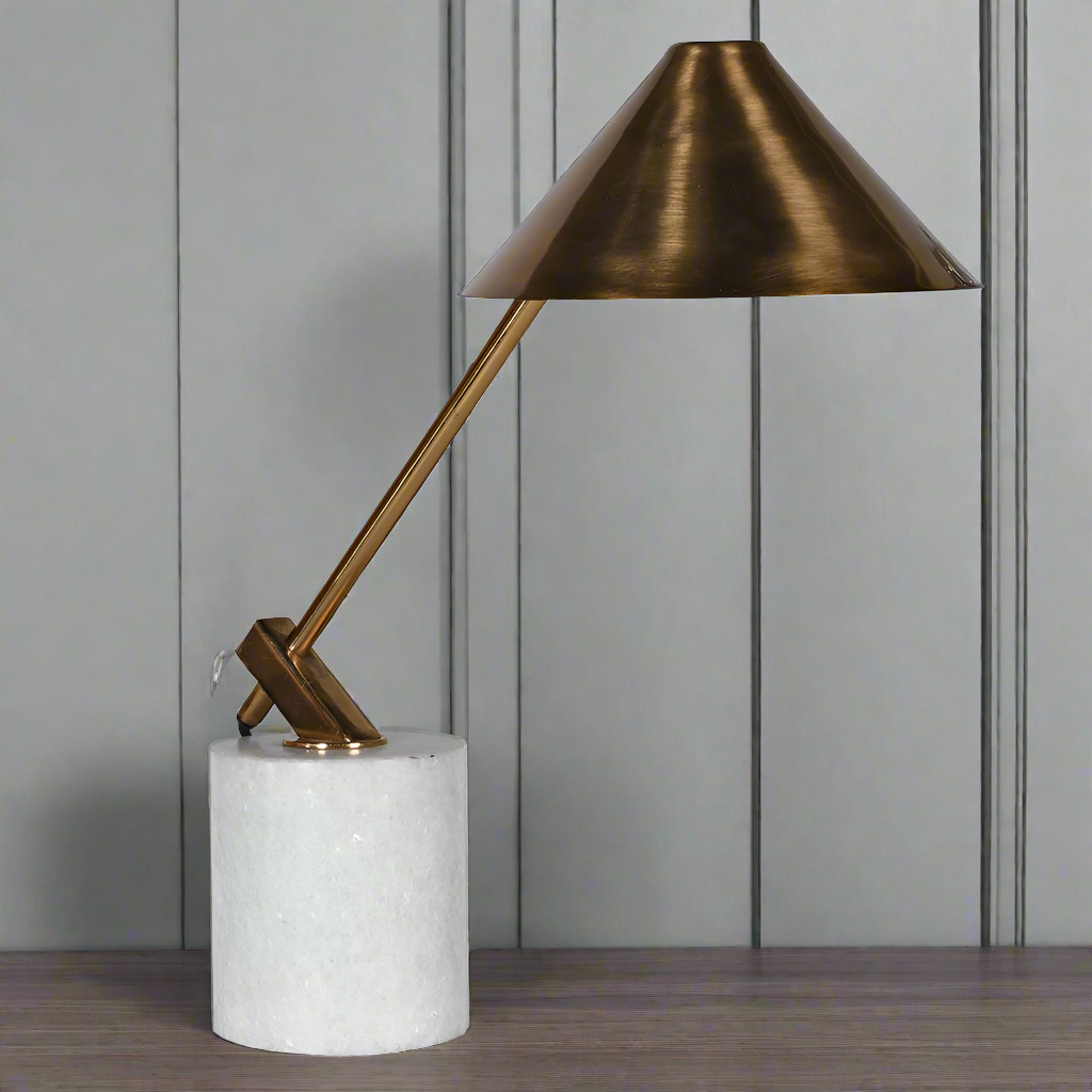 An antique brass desk lamp with a weighted marble column base, with a conical shade in a metallic finish.