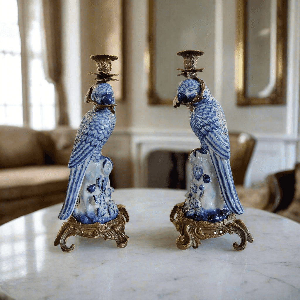 Pair of blue and white parrot candle holders on a marble surface with a blurred indoor background.