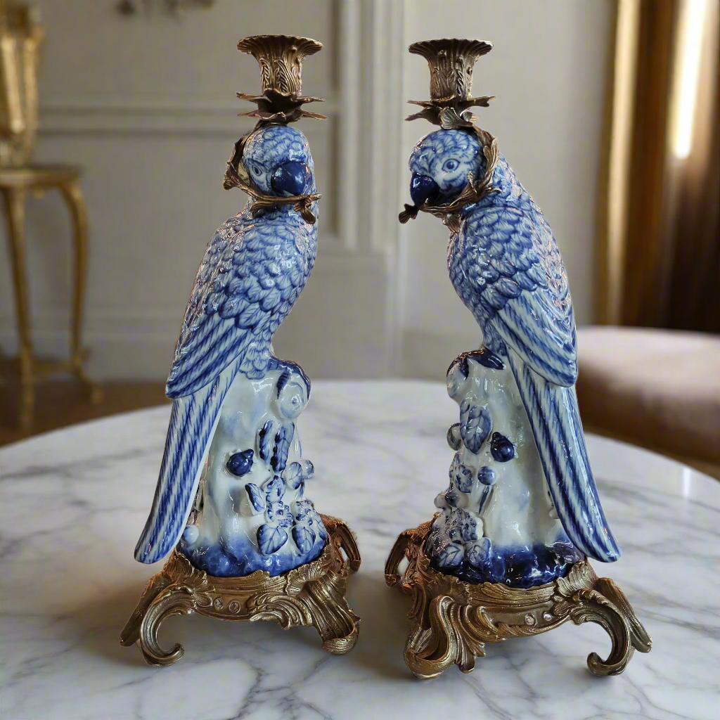Pair of blue and white ceramic parrot candle holders on a marble surface.