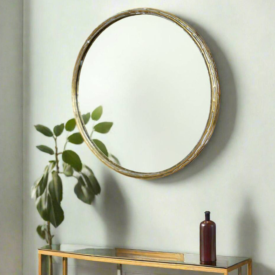 A round wall mirror with a distressed gold metal frame. The textured frame gives a vintage and rustic feel. 