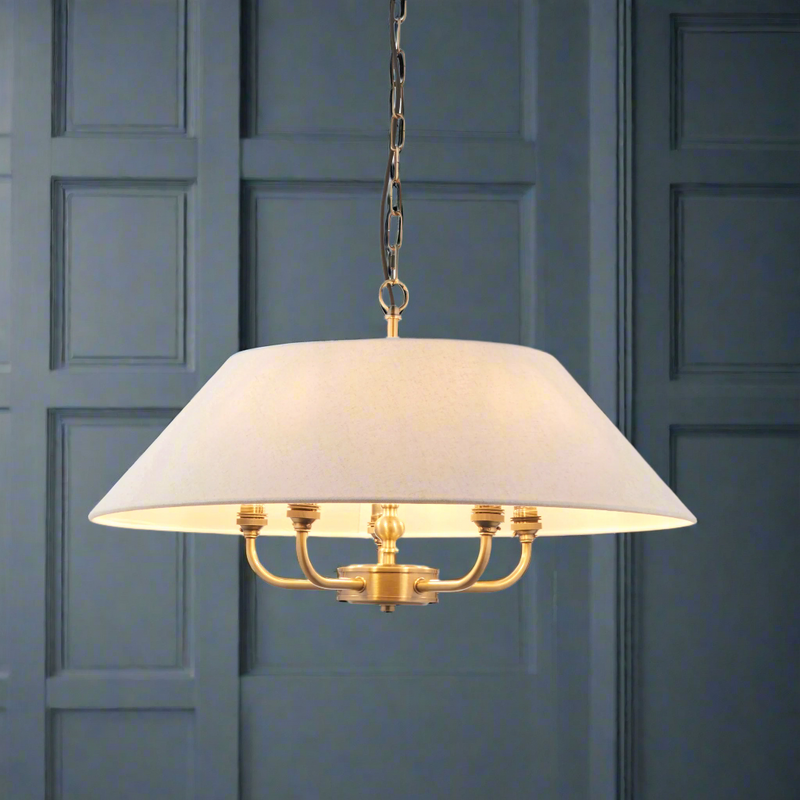 An elegant antique brass chandelier with a white linen shade, featuring five light bulbs, hanging from a gold chain.