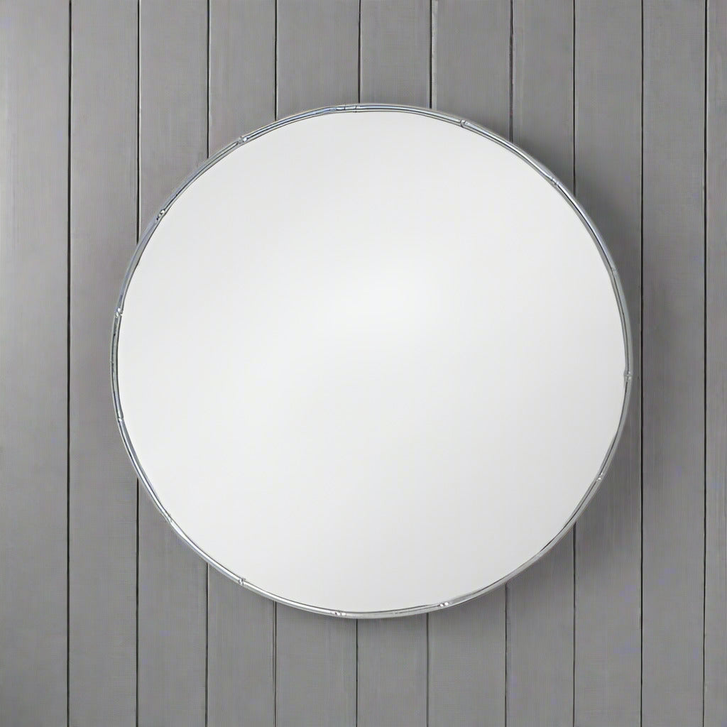 A decorative silver metal circular mirror with a bamboo frame, placed against a wooden background.