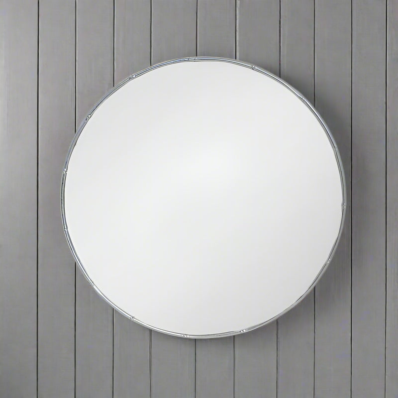 A decorative silver metal circular mirror with a bamboo frame, placed against a wooden background.