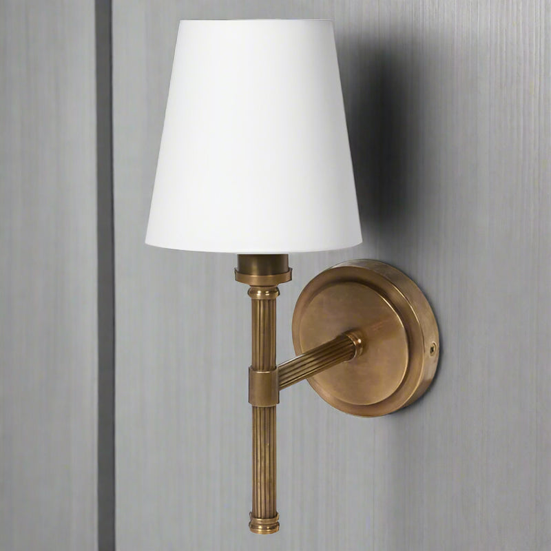 A single antique wall brass light with ribbed metal sconce and white linen shade.&nbsp; Perfect wall light for a bedroom, living room or hall.&nbsp; The antique brass finish works well in a country house or period town house interior.&nbsp;