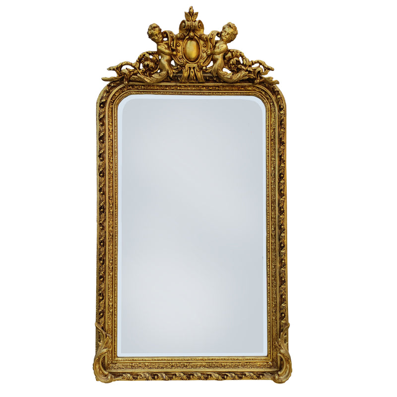 Ornate gilt wood wall mirror, with carved frame and topped with a pair of cherubs holding a medallion. Highly decorative mirror in the 'Georgian' style, perfect in a hall, over a fireplace in a living room or as a stunning addition to your bedroom or dressing room. These ornate wall mirrors work well in a period country home as well as adding that luxurious touch to a town home.

H: 180 cm W: 100 cm D: 16 cm