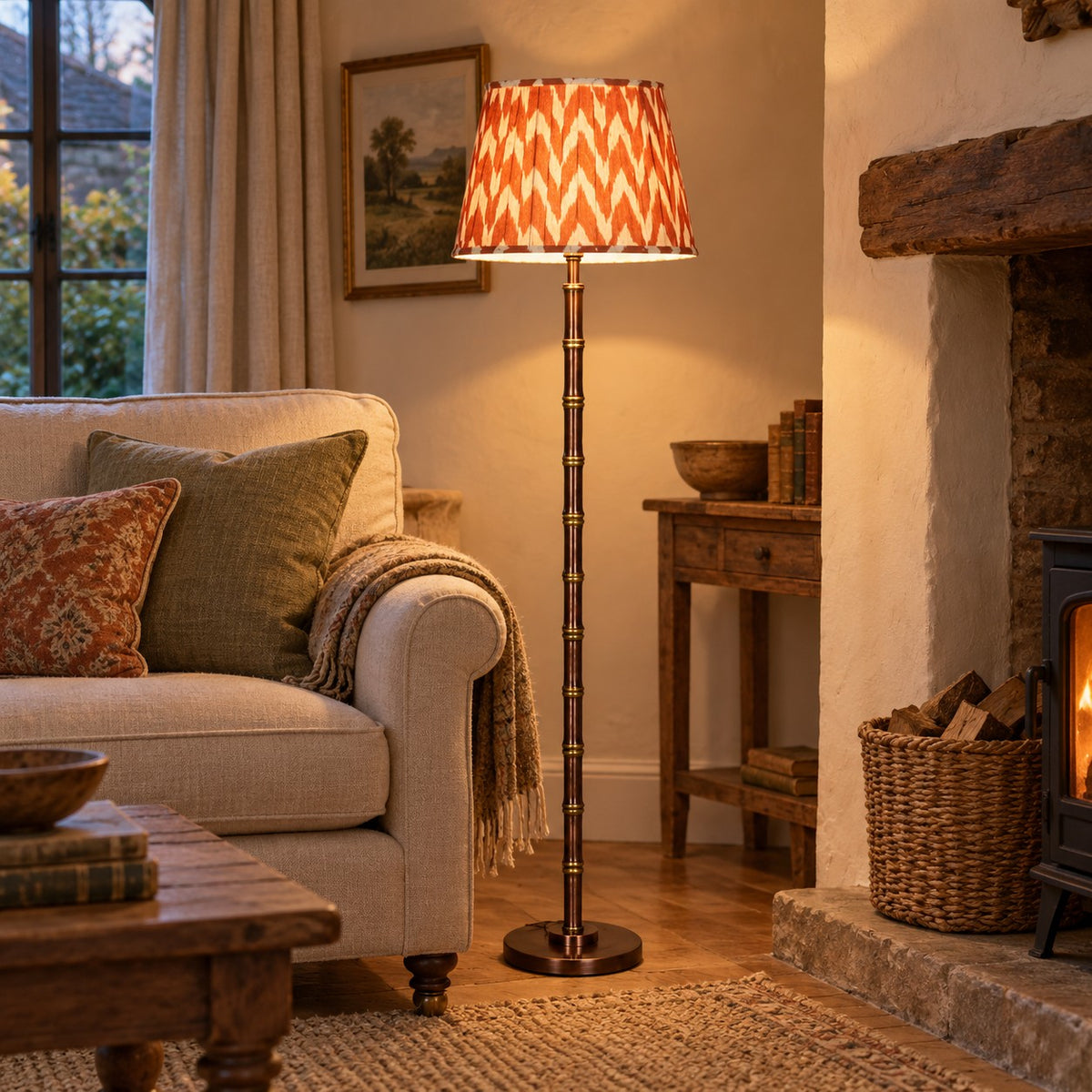 Faux bamboo metal floor lamp with rust and cream ikat-style shade lit beside a sofa in a country-style living room