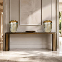 A modern console table with a brushed brass finish, styled in a bright entryway with two matching ceramic vases and a shallow bowl on top.