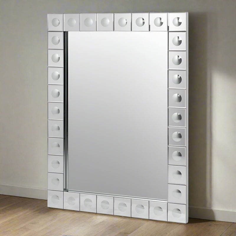 This is a Venetian-style wall mirror featuring a striking raised decorative frame. The rectangular mirror is bordered by a geometric design of square mirrored tiles, each accented with a raised circular dome detail that adds dimension, texture, and light-catching elegance. The reflective frame enhances the mirror’s brilliance, making it not only functional but also a bold decorative statement.

Its clean lines and sculptural frame give it a contemporary twist on classic Venetian design, making it versatile 
