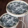 A very unusual set of two side tables, one nested below the other, circular tables on a white metal frame.&nbsp; The trays, which are detachable and can be used independently, have a traditional blue and white willow pattern style print on them. They are set off with a gold rim to the edge of the trays which lifts them and gives them a luxurious look. They combine modern minimalism with a classic scenic decorative top. Perfect in a contemporary setting, a cottage or period home.&nbsp;