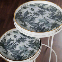 A very unusual set of two side tables, one nested below the other, circular tables on a white metal frame.&nbsp; The trays, which are detachable and can be used independently, have a traditional blue and white willow pattern style print on them. They are set off with a gold rim to the edge of the trays which lifts them and gives them a luxurious look. They combine modern minimalism with a classic scenic decorative top. Perfect in a contemporary setting, a cottage or period home.&nbsp;