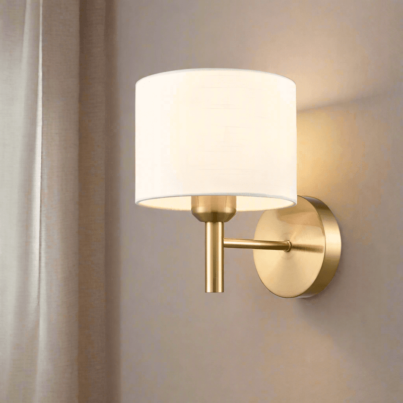 Aged brass wall light with cream shade in a bedroom