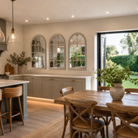Modern kitchen with wooden dining table and chairs, large mirrors on the wall, and a view of greenery outside.