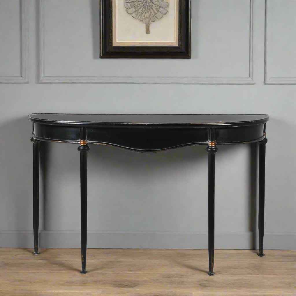 Metal console table with a slim black metal frame and a gracefully curved silhouette, 
distressed black finish with delicate gold accents in a hallway