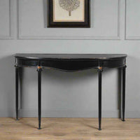Metal console table with a slim black metal frame and a gracefully curved silhouette, 
distressed black finish with delicate gold accents in a hallway