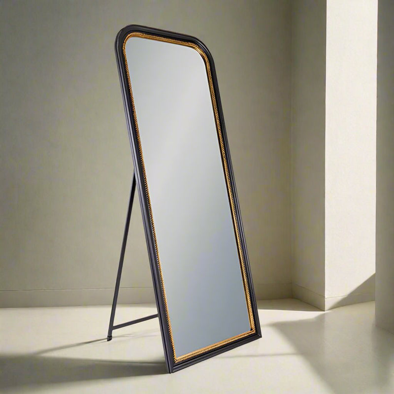 Black standing mirror by a window reflecting light into a room. 