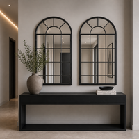 A pair of arched black window mirrors over  a console table in a contemporary hall.