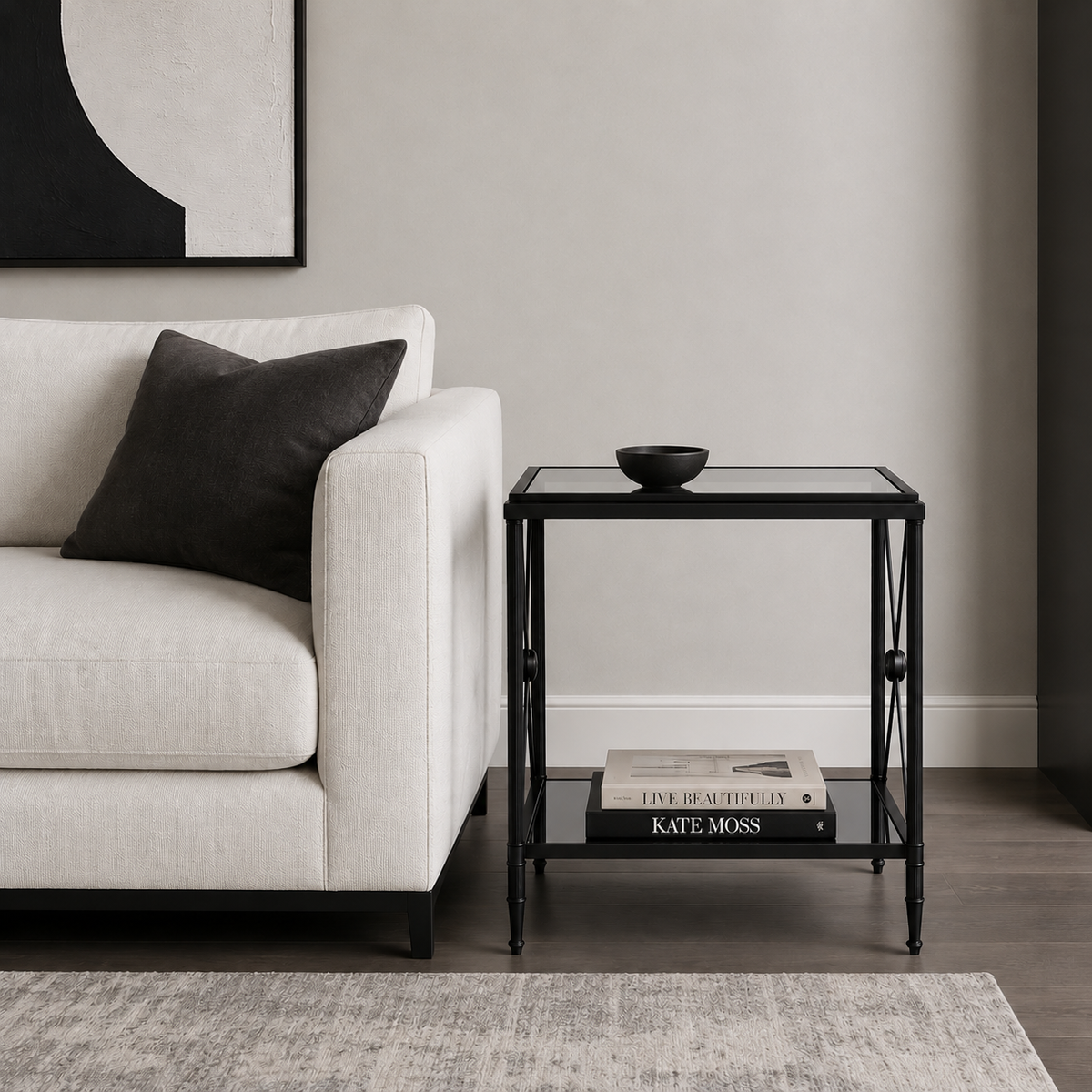 An empire style black metal and glass side table in a contemporary sitting room next to a white sofa.