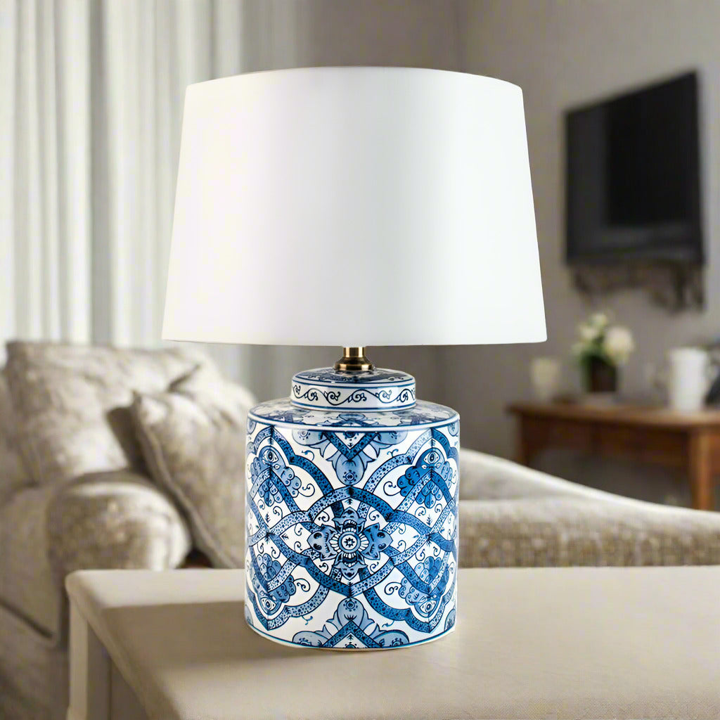 A blue and white ceramic lamp with a white shade, placed on a side table in a living room setting. 