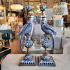 Decorative blue and white bird sculptures on a table with a blurred store background
