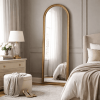 Tall, arched mirror, floor standing, leaning against a wall in a luxurious bedroom.