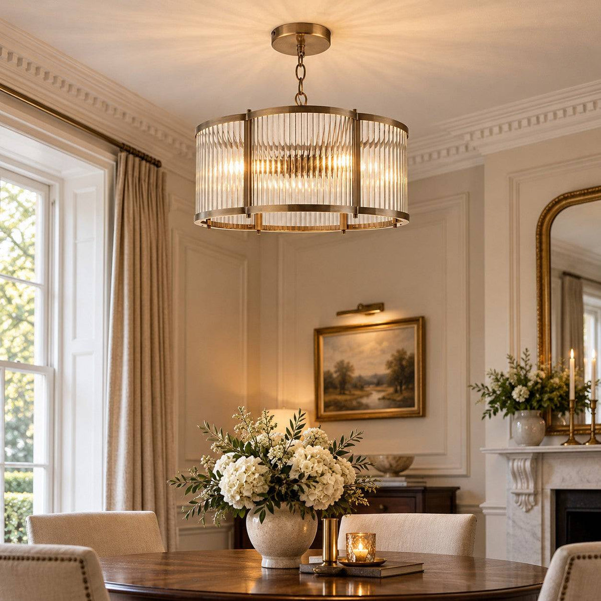 A modern cylindrical pendant light with a warm brass frame and ribbed glass shade hangs over a dining table in a beautifully decorated room with cream walls,