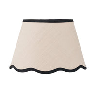 Cream tapered lampshade with scalloped bottom edge and contrasting black trim.