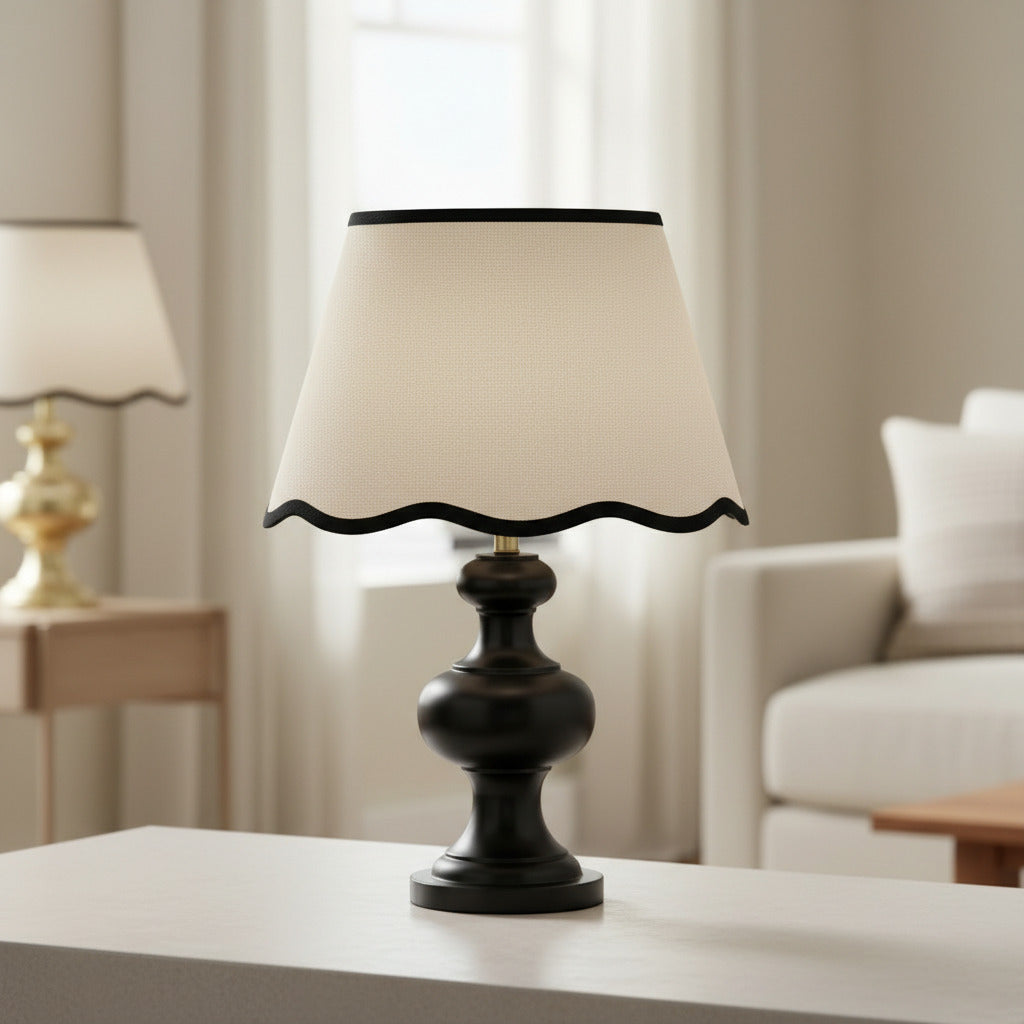 Cream tapered lampshade with scalloped bottom edge and contrasting black trim.