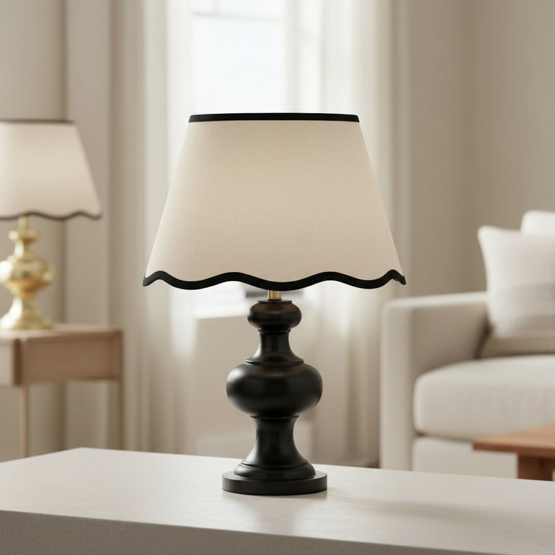 Cream tapered lampshade with scalloped bottom edge and contrasting black trim.