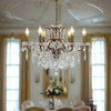 Six-arm bronze chandelier with crystal droplets and candle-style bulbs, hanging from a bronze chain, in a grand living room