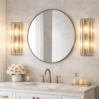 Crystal wall lights, lit either side of a bathroom vanity area, over a sink with brushed gold hardware.