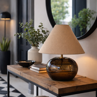 Smoked glass table lamp with rounded glass base and linen shade on wooden surface