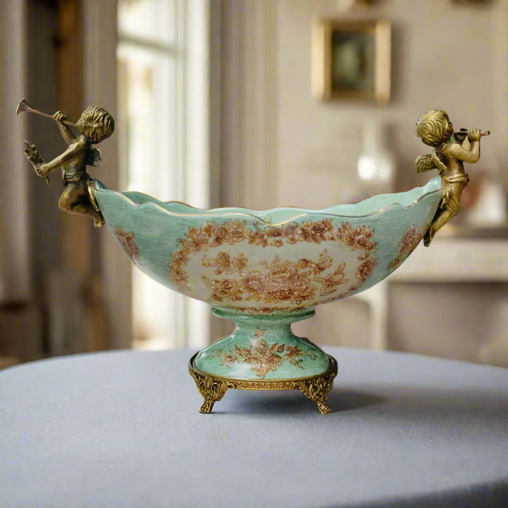 Lift your table decor with our stunning Bronze Cherub Porcelain Bowl, an heirloom piece and a masterpiece of craftsmanship and elegance. This beautiful bowl features intricate bronze cherubs adorning each end, resting delicately on tiny bronze feet.&nbsp;

Designed to impress, this Bronze and Porcelain bowl is more than just a functional piece - it's a work of art. The sloping scalloped edge adds a touch of sophistication, making it perfect for displaying fresh blooms, or even a bountiful arrangement of fru