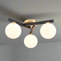 Modern low-profile flush mount ceiling light with three opal glass globe shades, matte black arms, and brushed brass accents in an asymmetric design.
