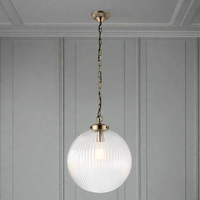 Antique brass and clear ribbed glass globe pendant light suspended from a decorative chain, showcasing a warm glowing bulb inside.