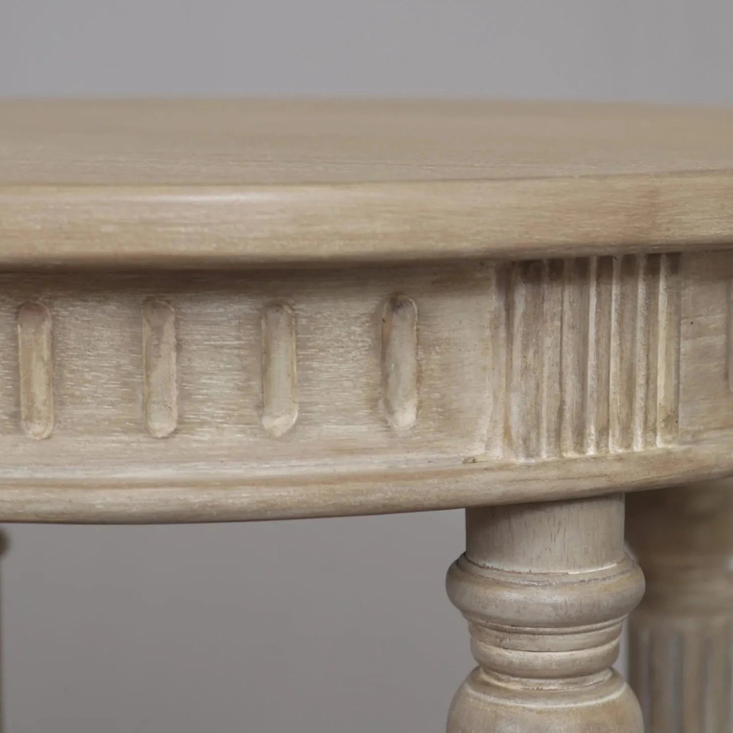 A vintage-inspired limewashed round wooden side table with turned fluted legs and a lower shelf, photographed against a neutral backdrop.