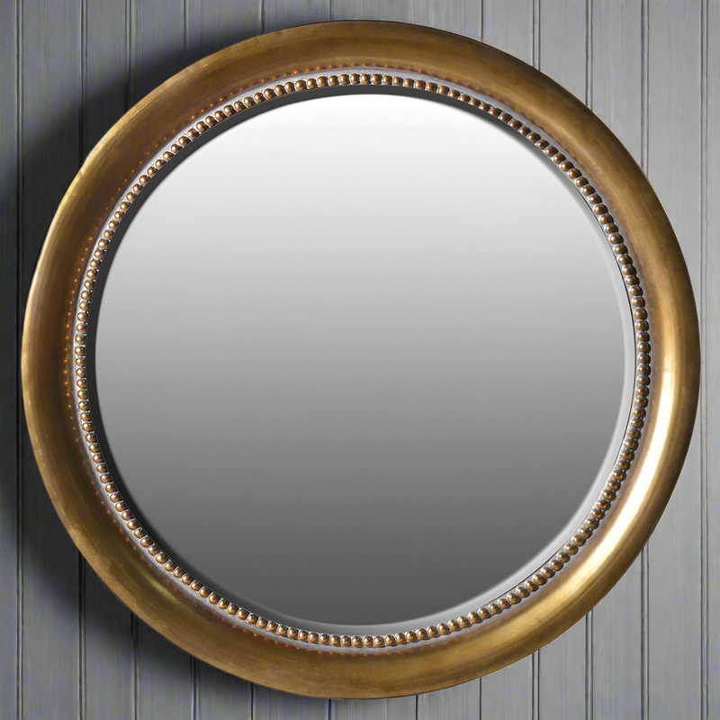 Large round metal wall mirror with antique brass frame and decorative beaded inner edge, ideal for classic or industrial interior designs.