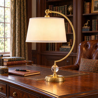 Curved brass arm and white shade desk lamp in a traditional study.