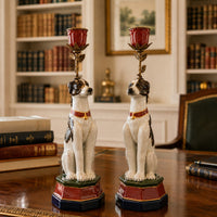 Pair of seated white porcelain dog candleholders with brown markings, red collars, colourful stepped bases and ornate floral stems holding red candle cups.