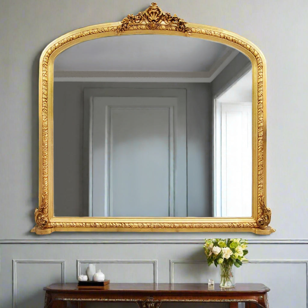 Ornate gilt overmantle mirror with a lavish gold leaf frame, decorative Rococo crest, and intricate baroque scrollwork – extra large size, styled for mantel or fireplace use.