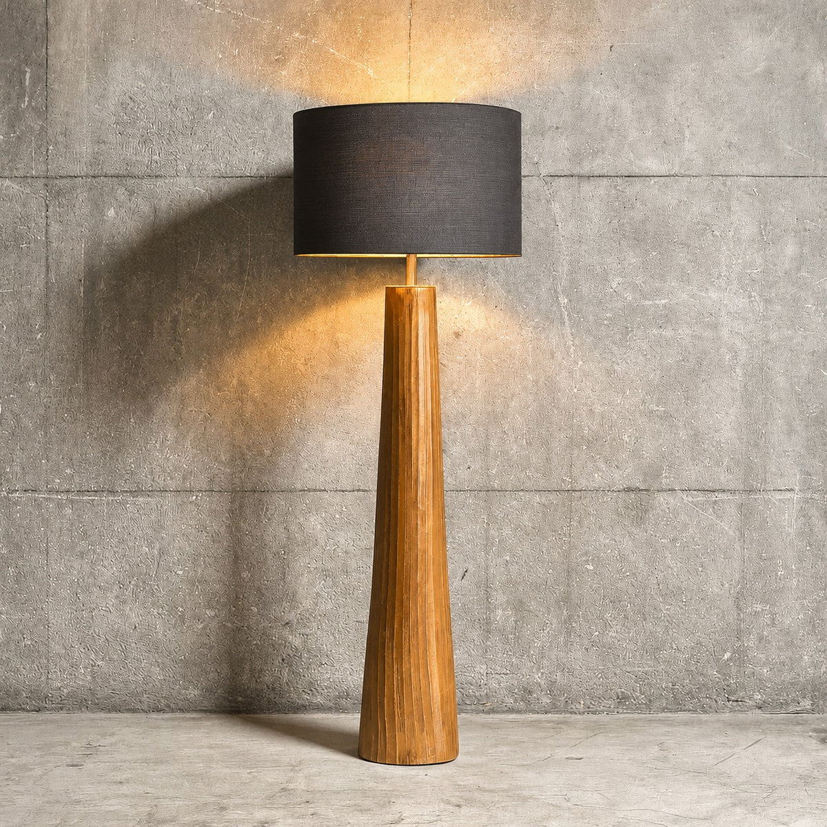 Floor lamp with wooden base and black shade against a concrete wall.