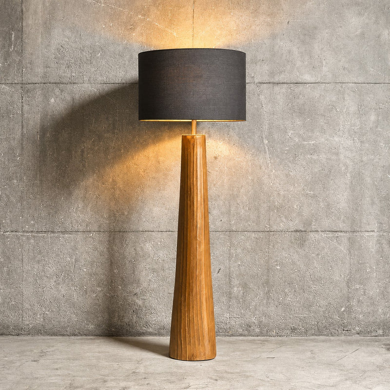 Floor lamp with wooden base and black shade against a concrete wall.