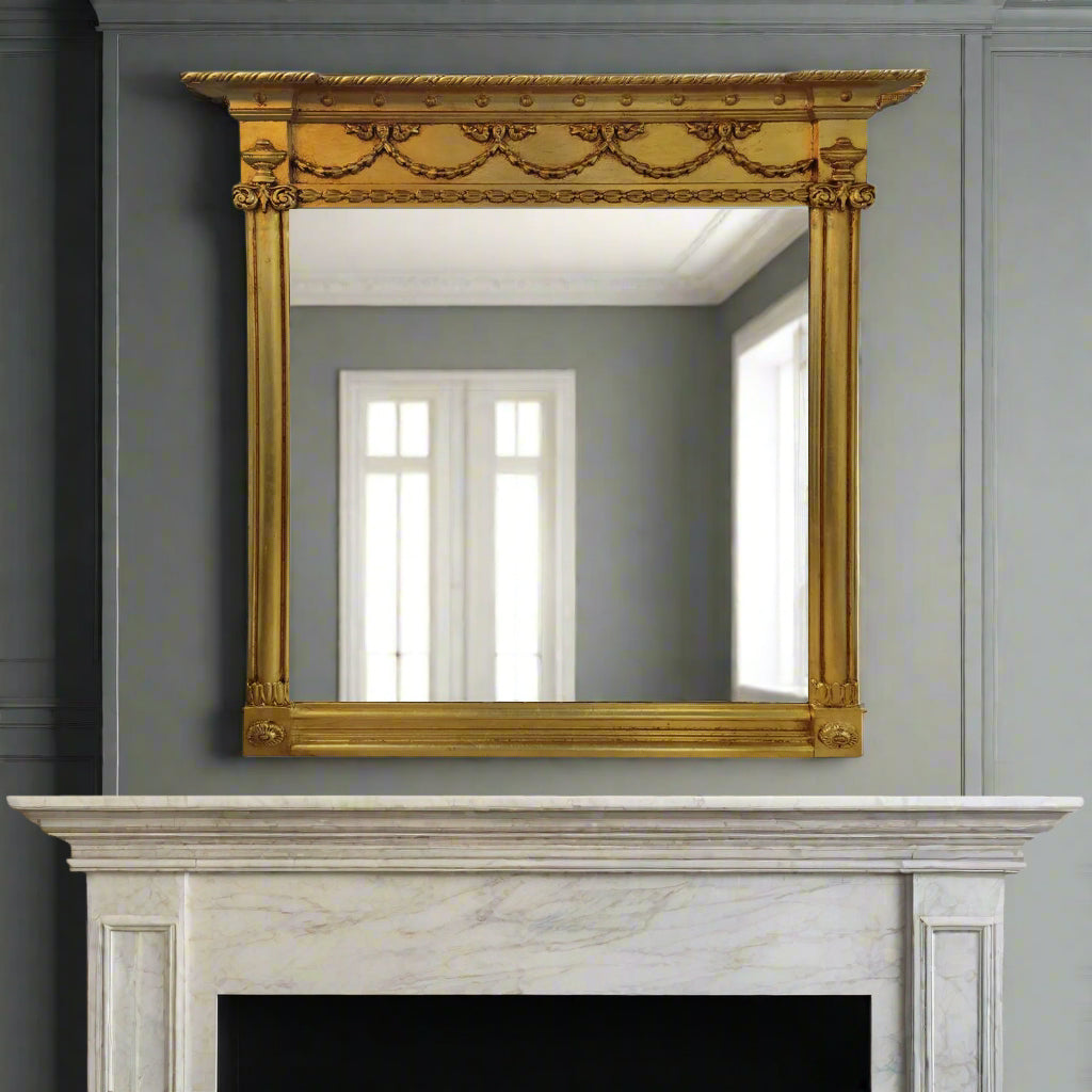 Decorative gold-framed, overmantle  mirror on a grey wall above a fireplace.