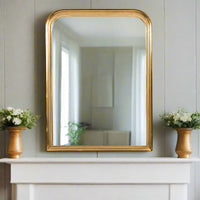 Gold beaded overmantle style mirror, classic shaped mirror over a wooden mantlepiece in a grey paneled room. 