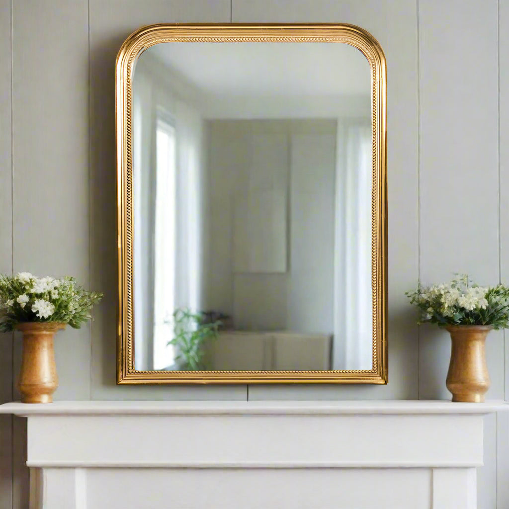 Gold beaded overmantle style mirror, classic shaped mirror over a wooden mantlepiece in a grey paneled room. 