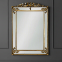 Exceptionally stunning statement mirror in gold, with beveled glass panels, gilt crown and corner gilt appliques on a grey panelled wall.