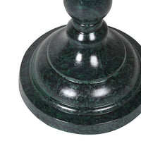 A slim very dark green, metal table lamp with a traditional design. It features a slender, ornate stand and a beige linen lampshade with a scalloped edge trimmed in blue. 