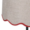 A slim dark green metal table lamp with a traditional design. It features a slender, ornate stand and a beige linen lampshade with a scalloped edge trimmed in red. 