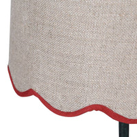 A slim dark green metal table lamp with a traditional design. It features a slender, ornate stand and a beige linen lampshade with a scalloped edge trimmed in red. 